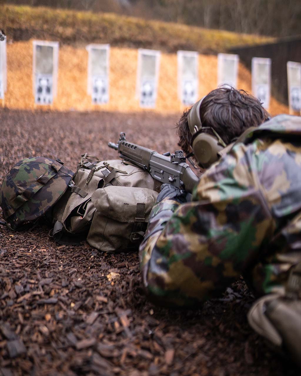 osoba strzelająca z karabinu do tarczy na strzelnicy leżąc na ziemi